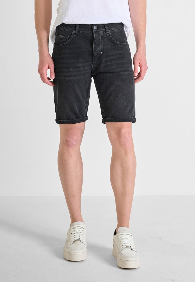 Shorts de mezclilla negra con dobladillos enrollados, diseño de cinco bolsillos y un ligero desgaste. Combinados con zapatillas blancas y una camiseta blanca sencilla.
