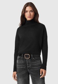 Suéter negro de punto con un cuello alto, puños acanalados, llevado sobre jeans grises que presentan un cinturón ancho negro con una hebilla geométrica dorada.