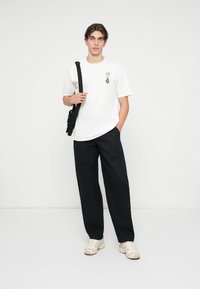 T-shirt blanche avec un design de rose rouge et de diamant noir, assortie à un pantalon noir ample et des baskets beiges. Sac à épaule simple.