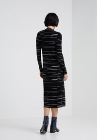 Abito nero a coste con strisce orizzontali bianche, maniche lunghe e lunghezza media. Da abbinare a stivaletti blu lucidi e tacchi.