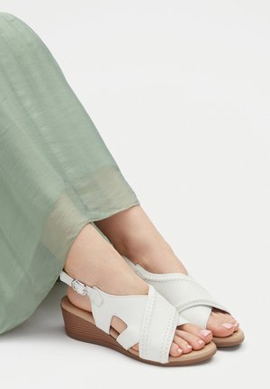 Weiße Keilsandaletten aus Leder mit Cut-out-Design und gesteppten Akzenten. Ausgestattet mit einem schlanken Knöchelriemen und einer strukturierten braunen Sohle.