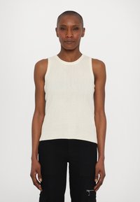 Top de tirantes acanalado en color blanco roto, diseño sin mangas, con un escote redondo. Combinado con pantalones negros que presentan un bolsillo lateral y detalle de cremallera.