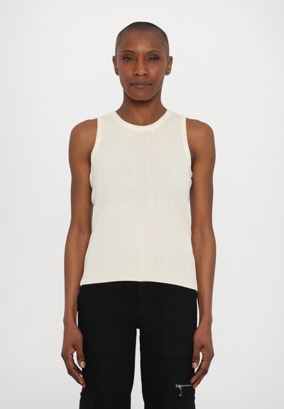Geribbelde tanktop in off-white, mouwloos ontwerp, met een ronde halslijn. Draagt met zwarte broek met een zijzak en ritsdetail.
