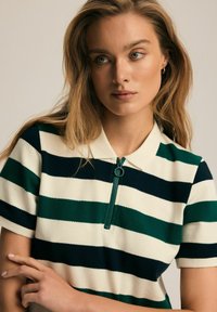Polo w paski w zielone i granatowe poziome paski, krótki rękaw, kołnierz oraz pół-zamek z okrągłym uchwytem.