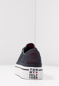 Schwarzer Textilsneaker mit roten Akzenten, verfügt über einen gemusterten Hinterteil, weiße Außensohle mit Logo und ein strukturiertes Obermaterial.