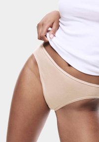 Intimo di cotone beige con una texture liscia, cintura elastica e delicati dettagli in picot, abbinato a un top bianco aderente.
