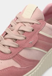 Ροζ σουέτ αθλητικό παπούτσι με υφή, λευκές λεπτομέρειες, επίπεδο κλείσιμο με κορδόνια και μικρή ασημένια λογότυπο.