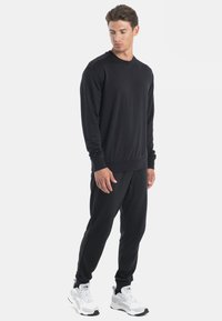 Schwarzer Sweatshirt und Jogginghose aus einem weichen, atmungsaktiven Stoff. Mit rundem Ausschnitt und elastischen Bündchen für zusätzlichen Komfort.