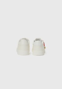 White sneakers with a smooth leather finish, rounded back, flat rubber sole, and decorative charm on the side. Minimalist design without patterns.