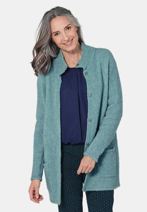 Un long cardigan bleu-vert clair en tissu doux et texturé. Il présente un col châle, une fermeture à boutons et deux poches avant.