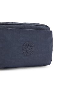 Navy blue fabric bag with textured surface and a circular logo patch. Features a zip closure and rectangular shape for structured storage.