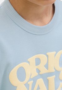 Helebeesinine sviiter, millel on kudumisega ümara kaelaava, millel on suur kollane trükitekst. Pehme kangas sileda tekstuuriga, mida rõhutavad julged tähed.