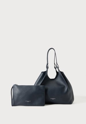 Sac à main en cuir noir texturé avec doubles poignées à côté d'une pochette assortie zippée, tous deux posés sur un fond clair uni.