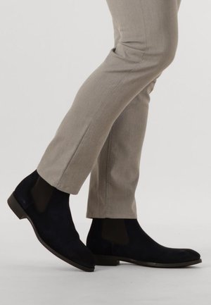 Zwarte suède enkellaarsjes met elastische zijkanten, platte hak en een strak ontwerp, gecombineerd met lichtgrijze op maat gemaakte broek.