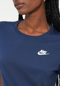 Námornícky modré bavlnené tričko s okrúhlym výstrihom a krátkymi rukávmi; obsahuje biele logo Nike na ľavej strane hrude.