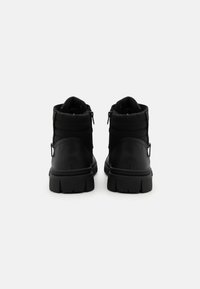 Botas negras hasta el tobillo con un exterior de cuero suave, cuello acolchado y cremalleras laterales. Suela de goma gruesa con un patrón de relieve.