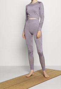 Fialová sportovní souprava obsahující krátký top s dlouhými rukávy a vysokým pasem legíny s texturovanými prvky a vzorovanými síťovanými detaily.