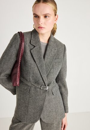 Grå hjernevæv blazer med bæltestropp og klapkrave, samt to frontlommer. Kombineret med en bordeaux lædertaske.