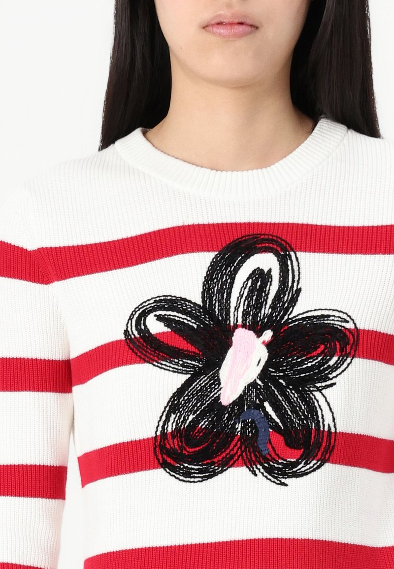 Weißer gestrickter Pullover mit roten horizontalen Streifen, der in der Mitte eine schwarze Blumenstickerei mit rosa und blauen Akzenten aufweist.