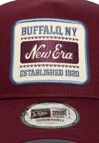 Burgunder basebollcaps med en broderad krämfärgad lapp i blå accenter, med texten "New Era" och "Buffalo, NY, Established 1920." Justerbar passform.