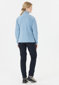 Vaaleansininen fleece-takki, jossa on korkea kaulus, yhdistettynä tummansinisiin housuihin. Takissa on sileä pinta, joka on täydellinen rentoon käyttöön.
