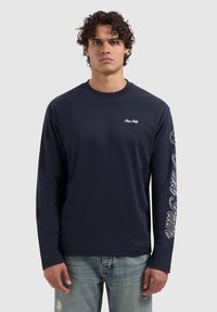 Navy langemouw t-shirt van katoen met een ronde hals. Bevat witte tekst op de rechtermouw en een klein logo op de linkerborst.