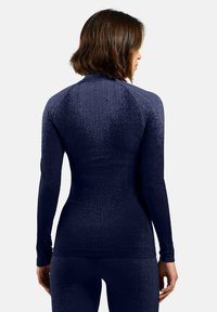 Haut de sport à manches longues bleu marine en tissu texturé, présentant une coupe ajustée, des manches raglan et un col montant.
