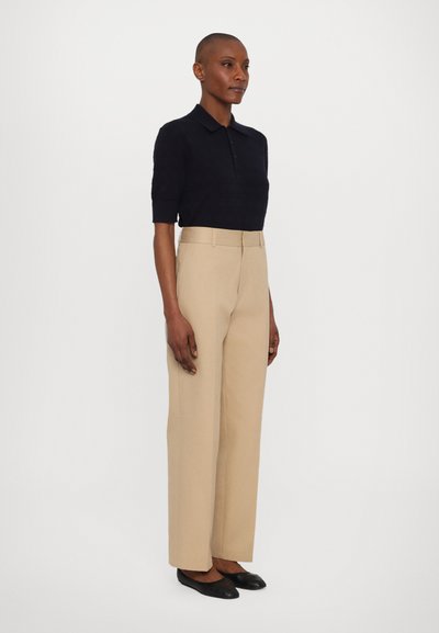 Cămașă polo de marină cu mâneci scurte, pantaloni largi bej și balerini negri. Design minimal, textură netedă și croi bine ajustat.