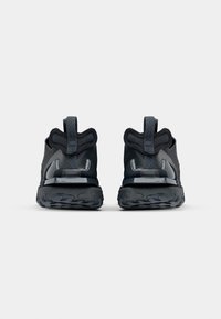 Paire de chaussures de sport noires vues de dos avec semelles texturées, languettes de talon rembourrées et une boucle en tissu en zigzag sur chaque chaussure.