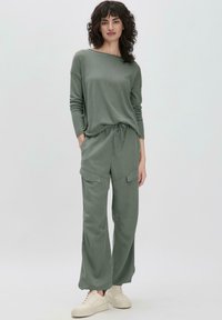 Haut long en coton vert avec un col bateau, associé à un pantalon cargo vert à coupe ample, doté de poches et d'une taille à cordon.