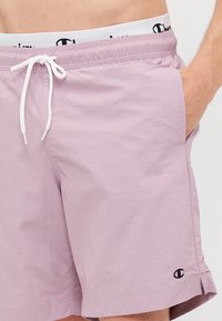 Șorturi de baie de culoare violet deschis, fabricate dintr-un material ușor, având un brâu elastic cu șnur, buzunare laterale și un detaliu mic cu logo.