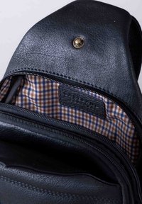 Black leather bag with a textured finish, featuring a zippered pocket and a brown and blue checked fabric lining. Hardware includes a circular snap.