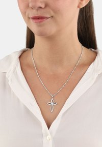 Collana d'argento con un design a catena attorcigliata, caratterizzata da un pendente a croce accentuato da pietre chiare rotonde. Indossata sopra una camicia bianca.