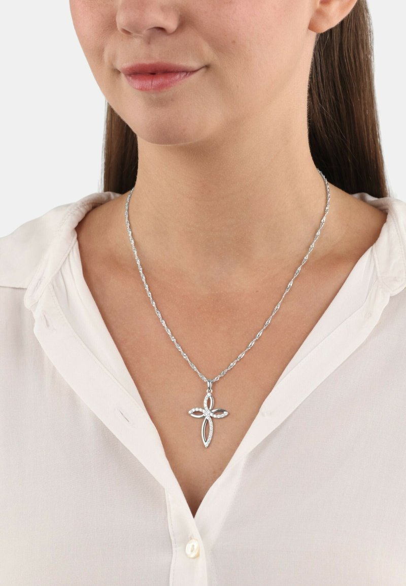 Collana d'argento con un design a catena attorcigliata, caratterizzata da un pendente a croce accentuato da pietre chiare rotonde. Indossata sopra una camicia bianca.