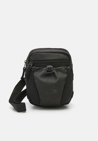 Kompaktowa czarna torebka na ramię z wieloma zamykanymi na zamek przegródkami, regulowanym paskiem oraz pętlą z klamrą na przedniej kieszeni.