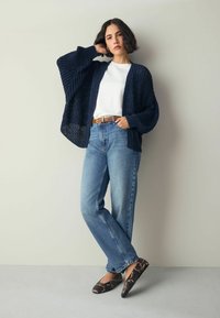Cardigan en tricot marine, chemise blanche, jean droit bleu clair et ballerines marron à imprimé serpent. Caractérisé par une coupe décontractée et un tricot texturé.