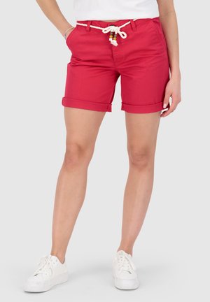 Rote Shorts mit umgeschlagenem Saum, Kordelgürtel und Perlendetails, getragen mit weißen Turnschuhen, von der Taille bis zu den Füßen an einer Person gezeigt.