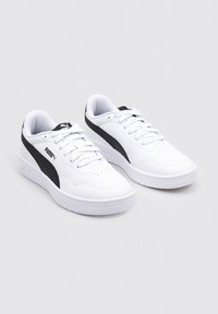 Zapatillas deportivas blancas con parte superior lisa similar al cuero, franja lateral negra texturizada, cordones en la parte delantera y puntera perforada para ventilación.