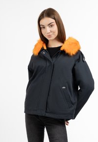 Giacca nera con un colletto in pelliccia arancione, dotata di chiusura con zip, tasche laterali e un logo sul lato sinistro. Texture liscia e design casual.