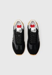 Sorte sneakers med en blanding av glatt og semsket tekstur, med en hvit etikett som har "LOVE MOSCHINO" og et rødt hjerte-design inni.