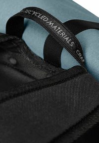 Une sangle noire avec le texte « Matériaux recyclés » sur une surface noire texturée, à côté d'un matériau bleu lisse, connectée au bord.