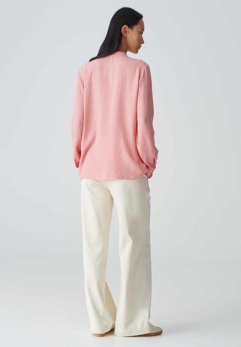 Rosa Leinenhemd mit einem lässigen Schnitt, langen Ärmeln und Knopfdetails, kombiniert mit cremefarbenen weiten Hosen und beigen Schuhen.