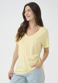 Žuta V-neck majica od mekog, laganog materijala. Kratki rukavi, ležeran kroj i suptilna tekstura. Nosena uz svijetloplave traperice.
