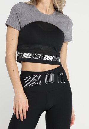 Frau trägt ein graues und schwarzes Nike-Crop-Top und schwarze Leggings mit der Aufschrift "JUST DO IT." am Bund.
