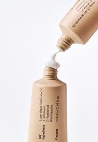 Beige tube die witte crème aanbrengt op de opening van een andere tube, gelabeld met ingrediënten voor huidverzorging en netto volume.