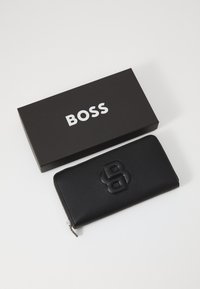 Black leather wallet with textured surface and embossed logo, placed next to a black box featuring the brand name in white.