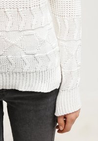 Biały sweter z dzianiny z fakturowanymi wzorami, z prążkowanym dołem i mankietami. Lekki, z otwartym ściegiem, prezentujący swobodną sylwetkę.