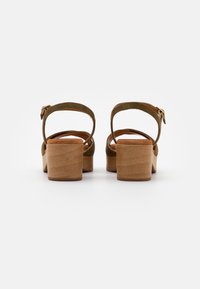 Sandales à talons en suède vert avec un large talon en bois, une bride de cheville ajustable et une doublure intérieure lisse.