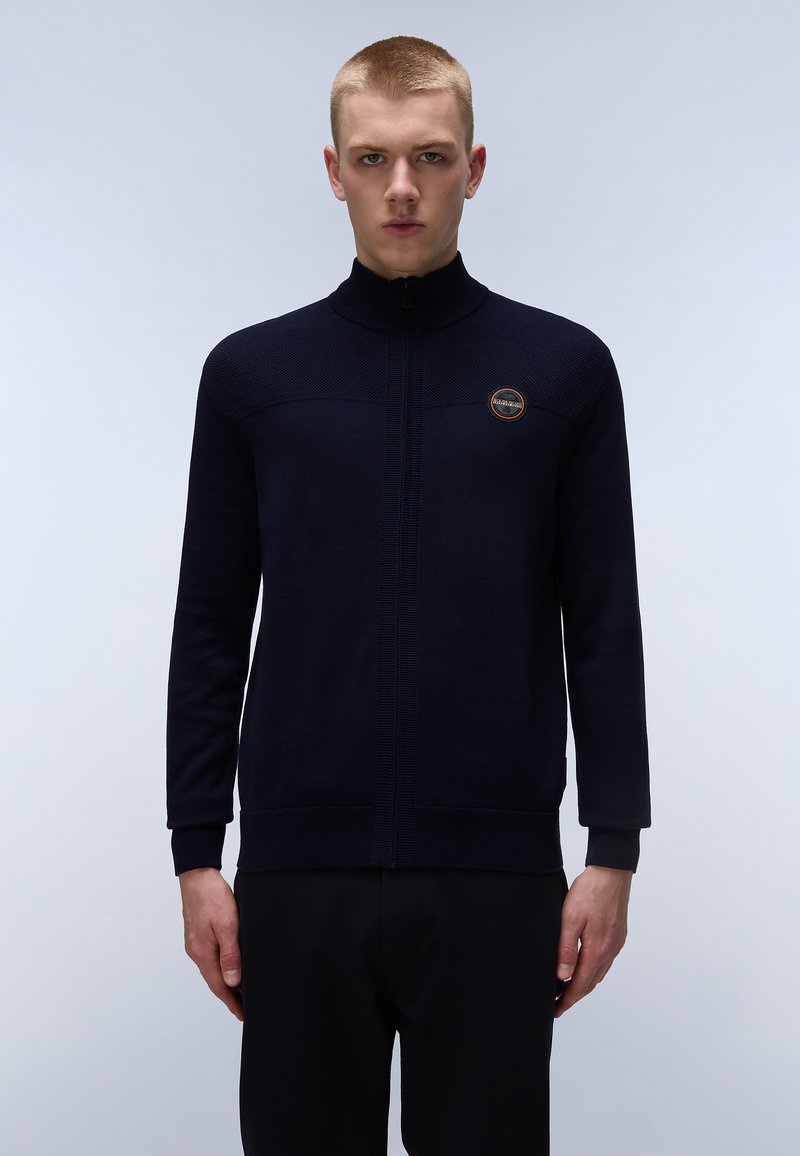 Pull en laine bleu marine à fermeture éclair avec col haut, panneau supérieur texturé, manches et ourlet côtelés. Arbore un logo rond sur la poitrine gauche. Tissu en tricot lisse.