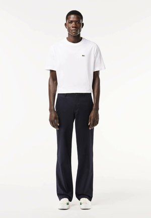 White cotton T-shirt, short sleeves, crew neck; navy trousers, straight-leg, smooth fabric, paired with white sneakers featuring green accents.